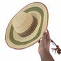 Hand holding a woven straw hat with a decorative band on a textured surface