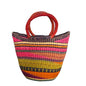 A hand-woven straw tote bag with vibrant multicolored vertical stripes in pink, orange, yellow, green, and purple, featuring two thick reddish-brown woven handles.