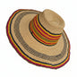A natural straw sun hat with a wide brim, featuring woven stripes of black, red, yellow, and beige around the crown and brim edge, shown being worn on a person's head.