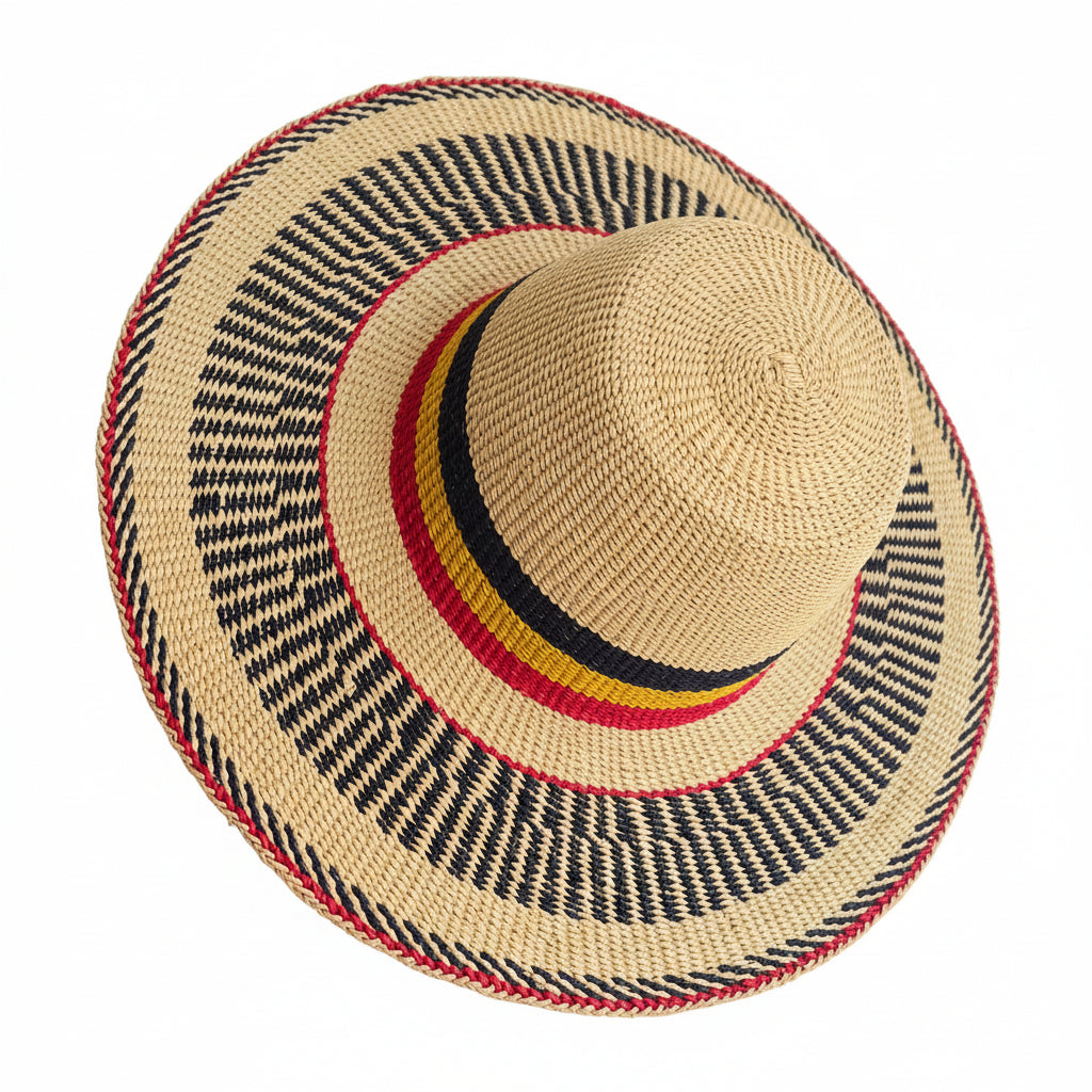 A woven straw sun hat with a wide brim, featuring black, red, and yellow stripes on the crown band and brim edge, held by a hand on a dark counter.