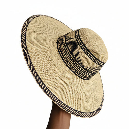 A woven straw sun hat with a wide brim and a black patterned band, shown resting on a shelf in what appears to be a workshop or storage area.