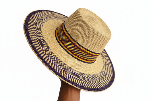 A wide-brimmed straw hat with a natural beige crown and brim, featuring a dark purple woven band and a central decorative band with yellow, orange, and red stripes. A hand is holding the brim on the right side.