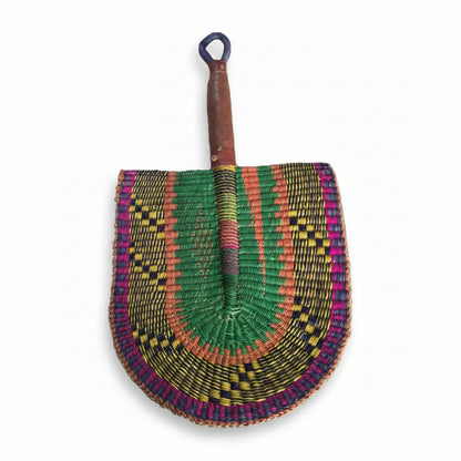 A hand-woven semicircular fan with a wooden handle, featuring intricate geometric patterns in green, pink, orange, yellow, and purple, displayed on a white plastic tray.