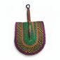 A hand-woven semicircular fan with a wooden handle, featuring intricate geometric patterns in green, pink, orange, yellow, and purple, displayed on a white plastic tray.