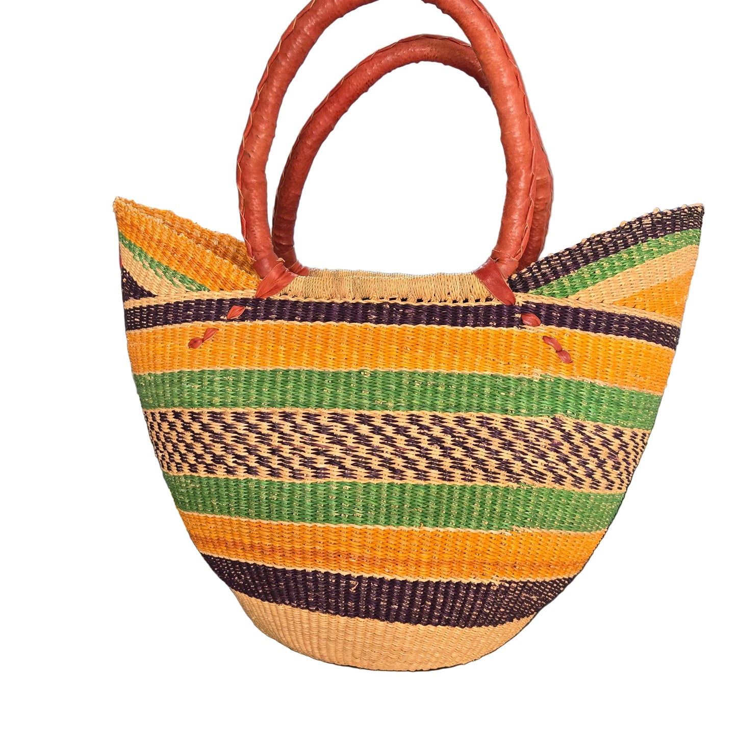 A woven straw tote bag with vertical stripes in yellow, green, brown, and beige, featuring two brown leather handles, photographed on a desk.