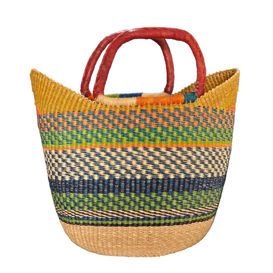 A woven basket bag with a natural tan base, multicolored striped patterns in green, blue, yellow, and orange, and reddish-brown double handles, photographed in an office-like setting.