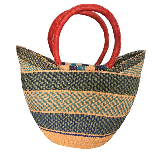 A woven straw tote bag with dark green and beige stripes and thick red handles, photographed on a desk with office items in the background.
