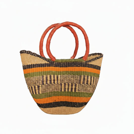 A woven straw tote bag with orange-red handles, featuring vertical stripes of orange, olive green, black, and natural beige, photographed on a desk in an office setting.